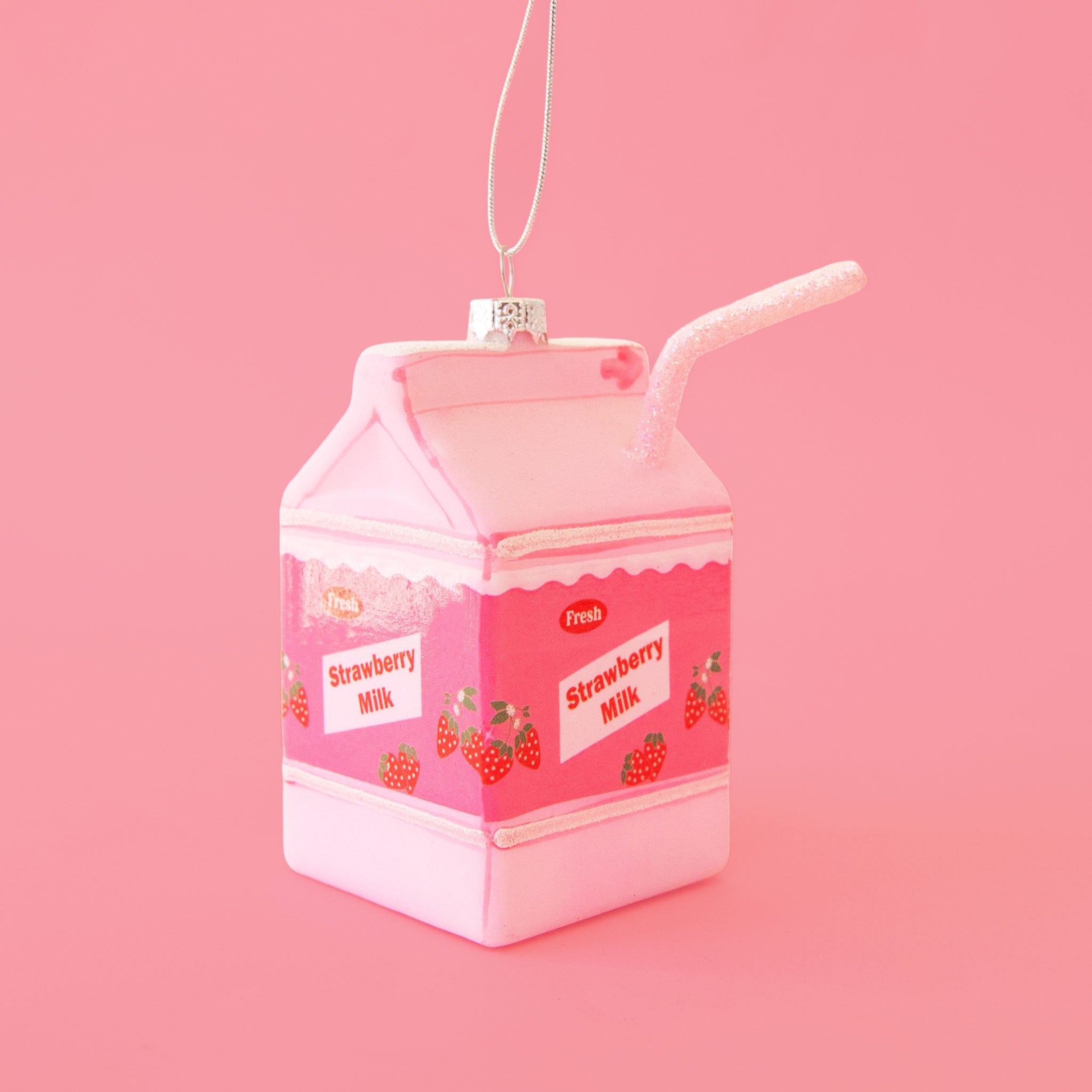 A pink glass strawberry milk carton shaped ornament with text that reads, 'Fresh Strawberry Milk'. 