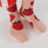 On a white background is a model wearing pink crew socks with a red strawberry pattern on it. 