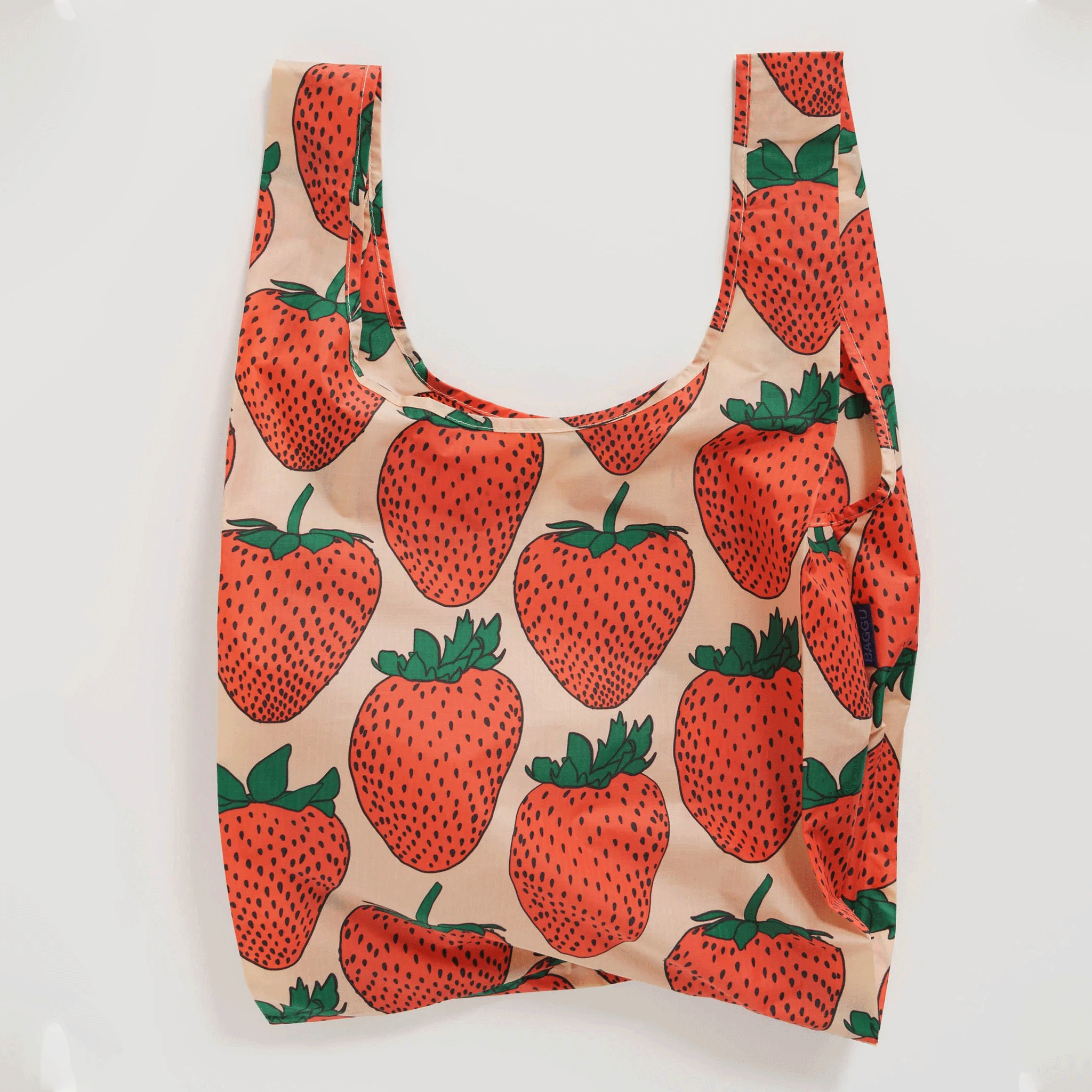 On a white background is a light pink and red strawberry patterned nylon tote bag. 