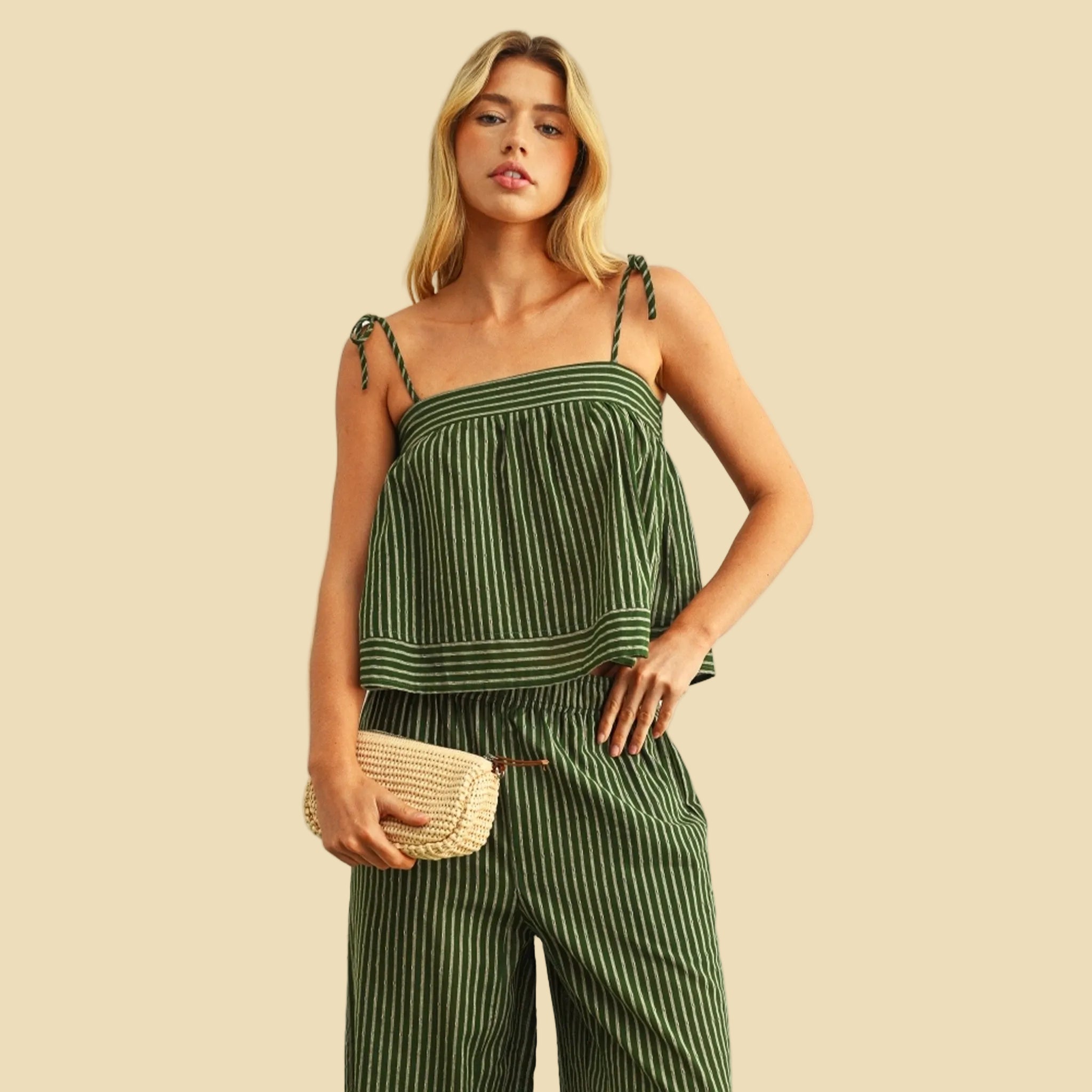 Woman wearing a green striped jumpsuit holding a clutch against a plain background
