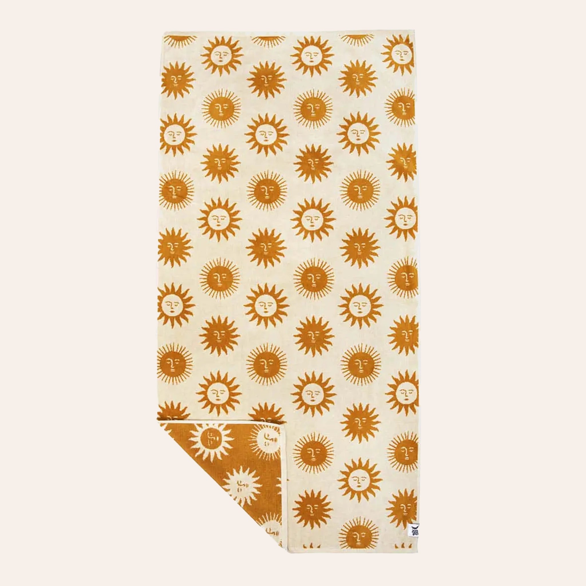 A cream and mustard yellow beach / bath towel with a sun design on the front and back, photographed here with the cream side facing up and a corner of the towel flipped over to show the opposite yellow side. 