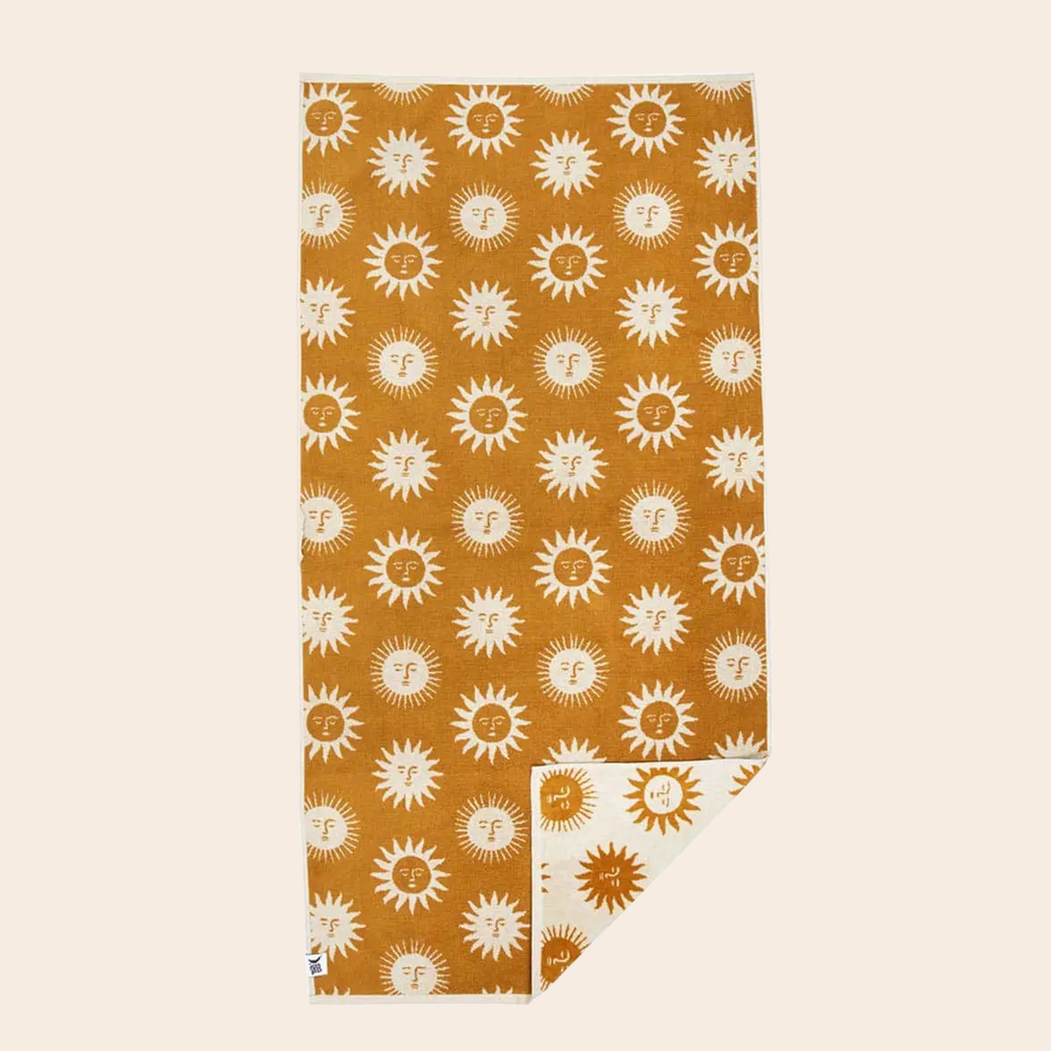 A cream and mustard yellow beach / bath towel with a sun design on the front and back, photographed here with the mustard side facing up and a corner of the towel flipped over to show the opposite cream side. 
