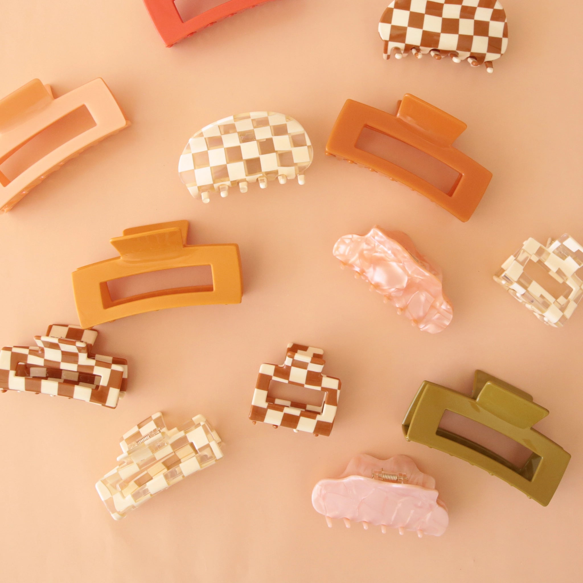 On a peachy background is an assortment of claw clips in different shapes and sizes. 