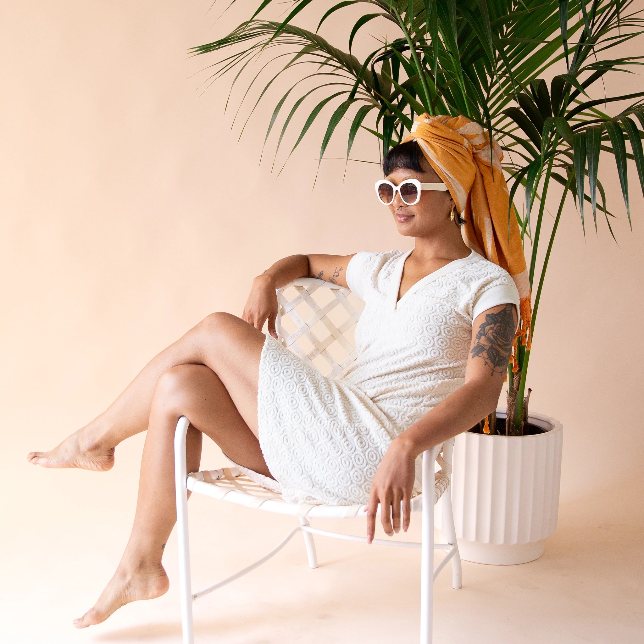 A model sitting on a chair in front of a palm tree wearing the Retro Flower Beach Towel around their head. 