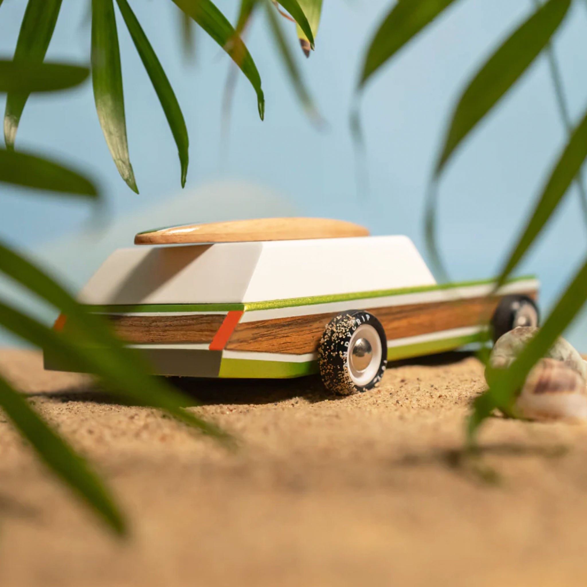 Small surf toy vehicle on sand with leaves in foreground