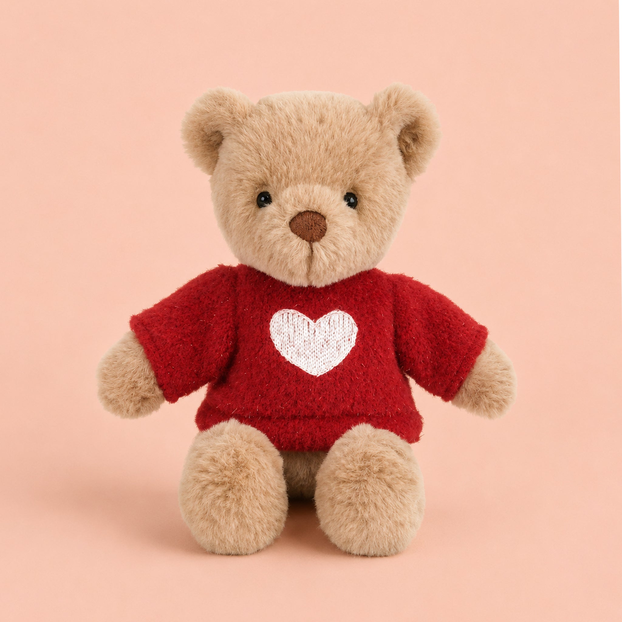 A little bear stuffed animal toy wearing a red sweater with a white heart in the center. 