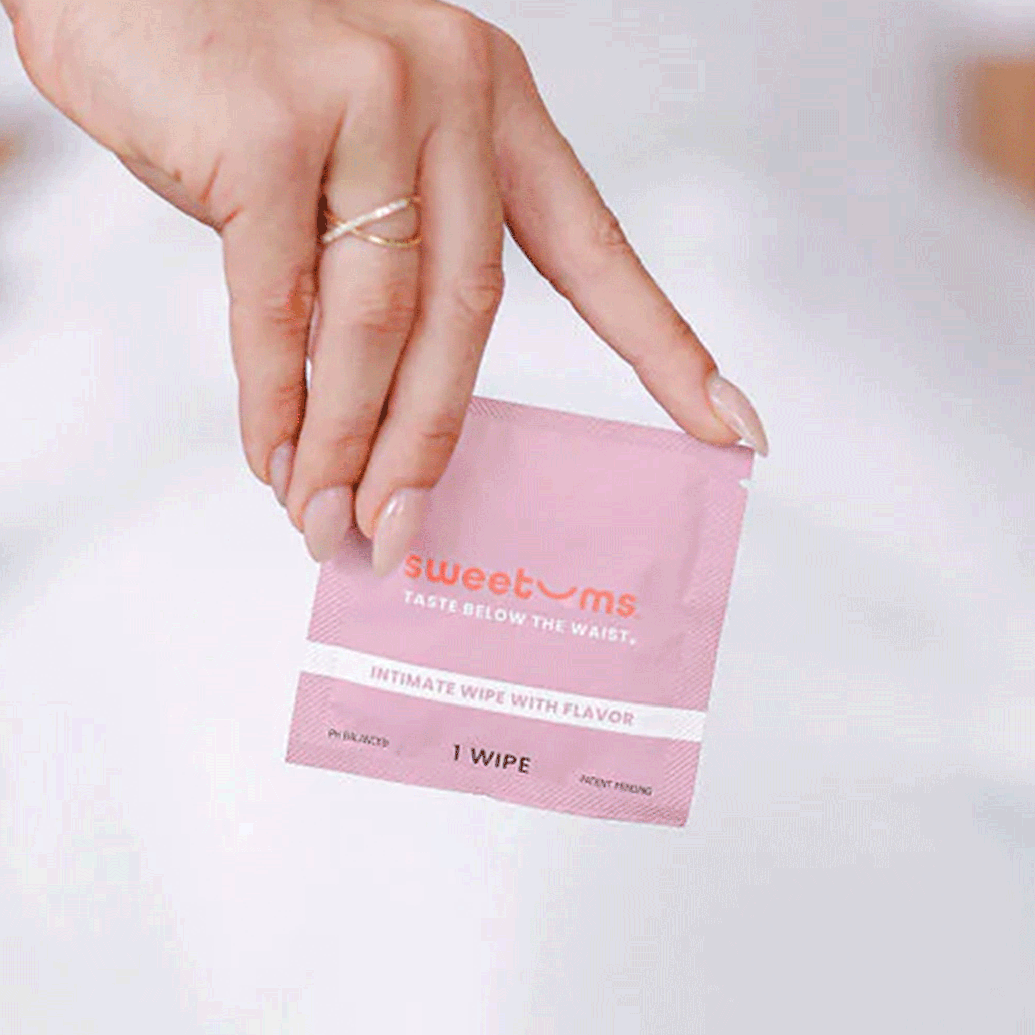 On a white background is a hot pink packet of a feminine wipes with text on the front that reads, &quot;sweetums taste below the waist intimate wipe with flavor&quot;.