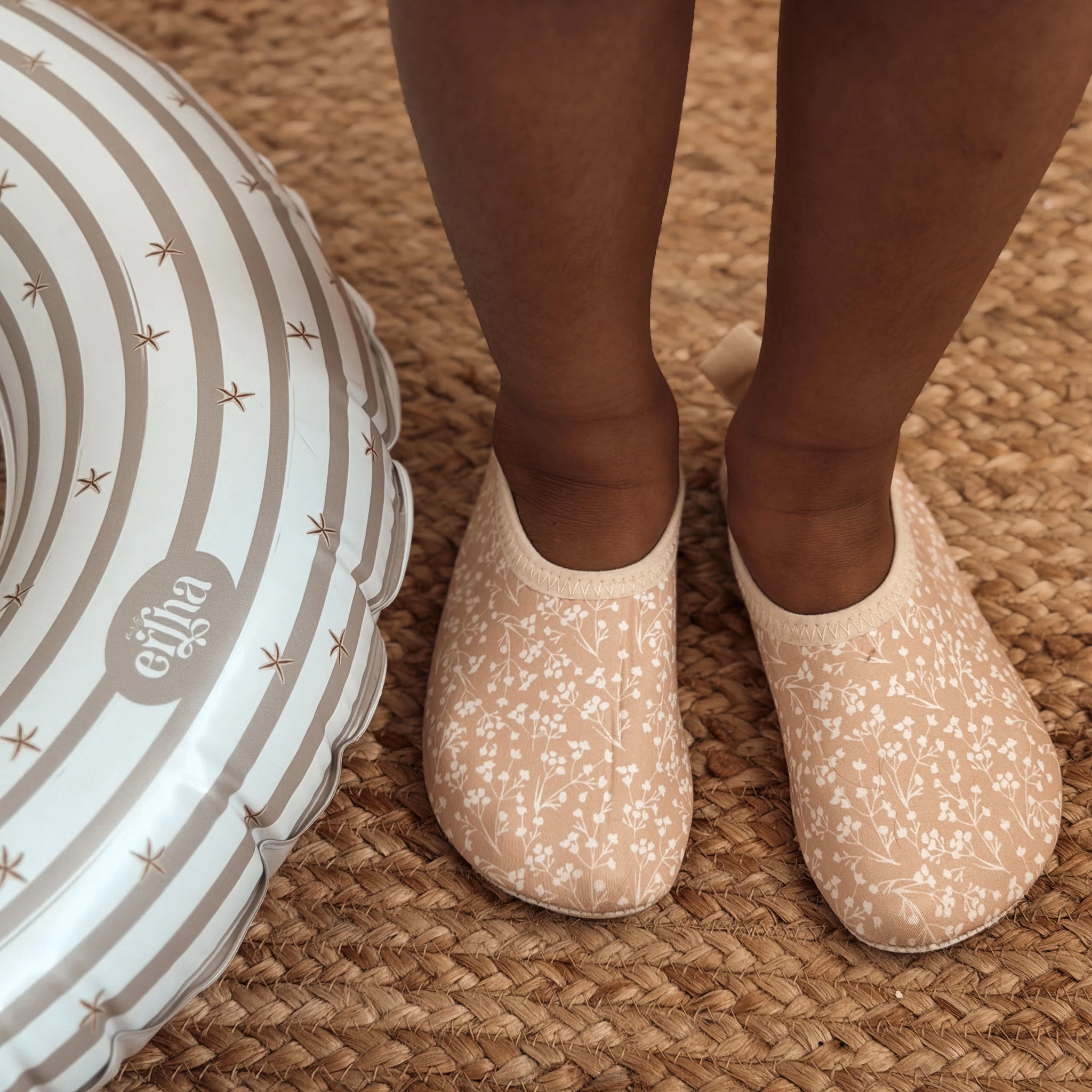 Pair of peachy/tan swimming shoes with floral pattern on a beige background