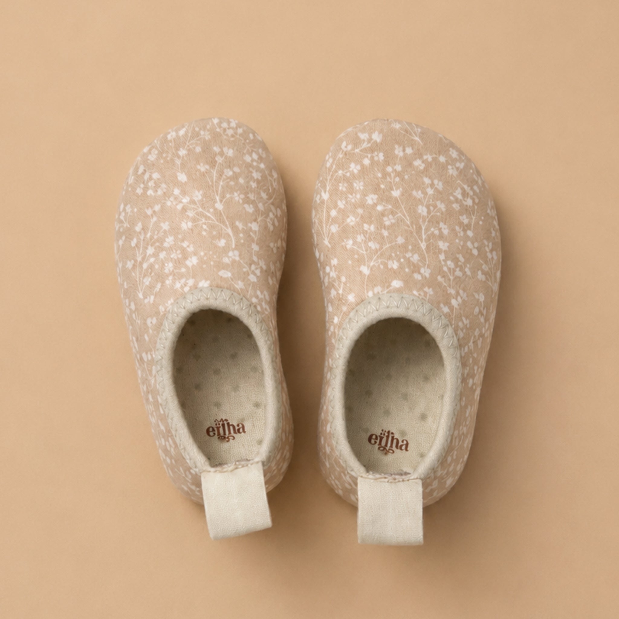 Pair of peachy/tan swimming shoes with floral pattern on a beige background
