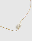 A dainty gold necklace with a single pearl bead in the center. 