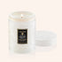 A glass candle with beautiful etched details sits in the middle of image.  Candle label reads "Voluspa Tahitian Coconut Vanilla"