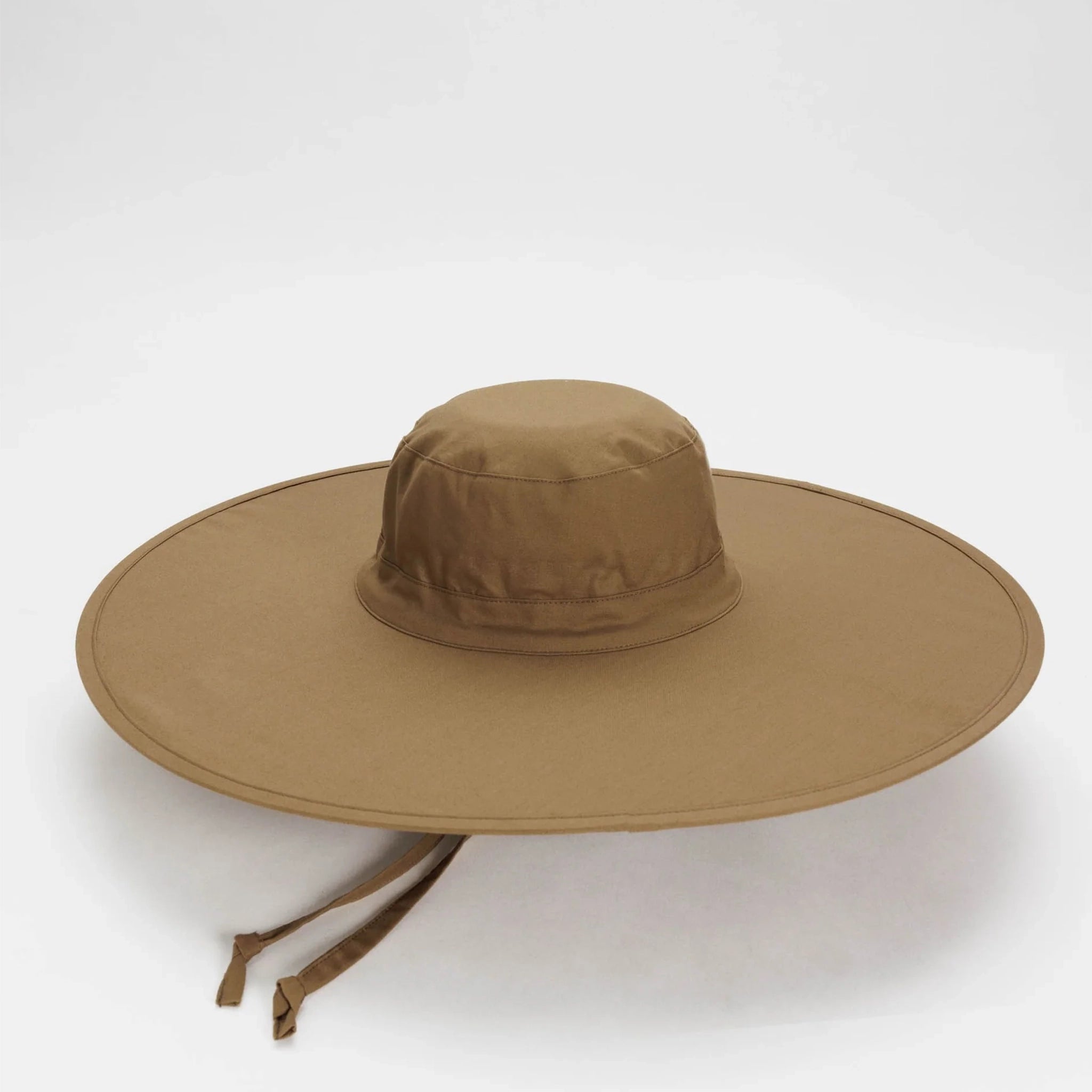On a white background is a packable sun hat in a brown shade that has an extra large brim, two straps for securing and folds down to a compact size for easy on the go travel. 
