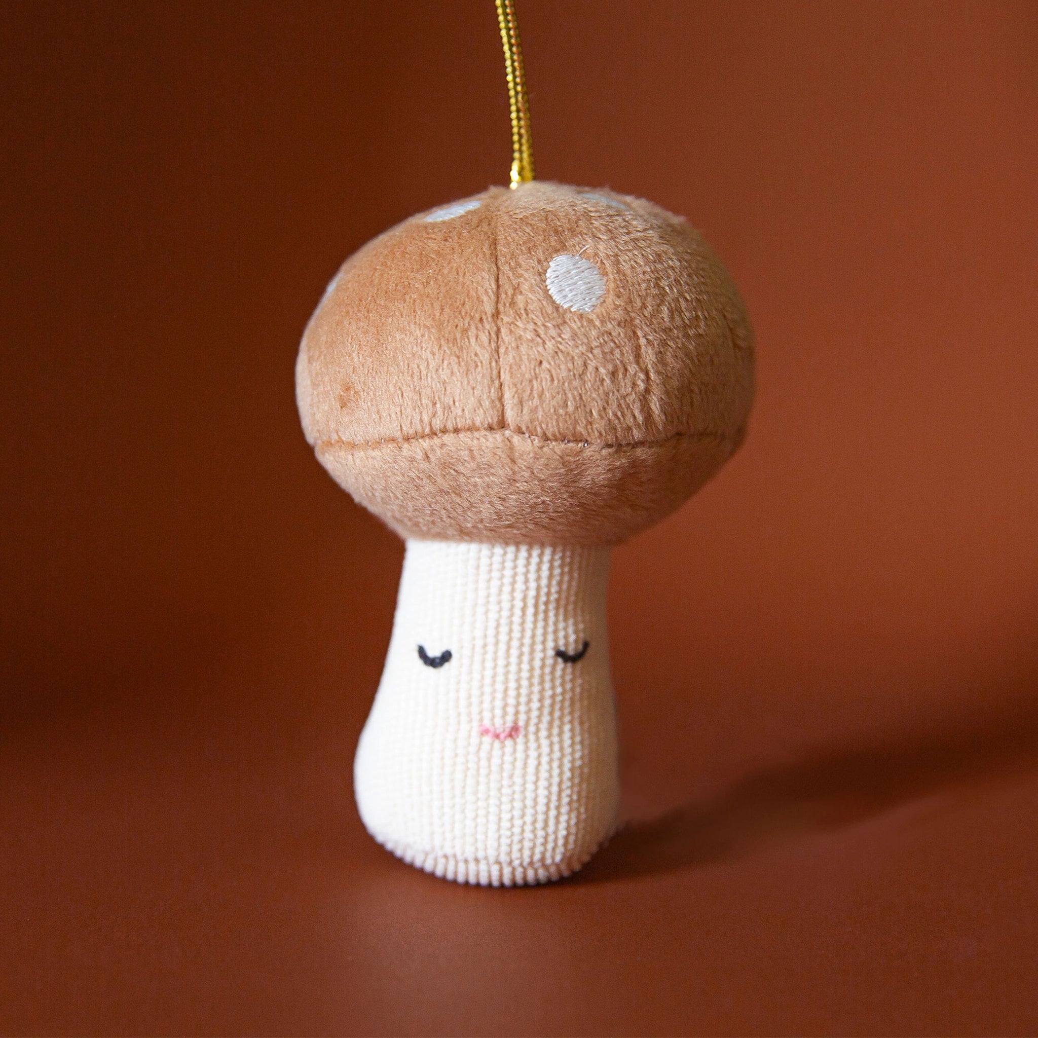 On a burnt orange background is a tan and cream mushroom ornament with an adorable expression.