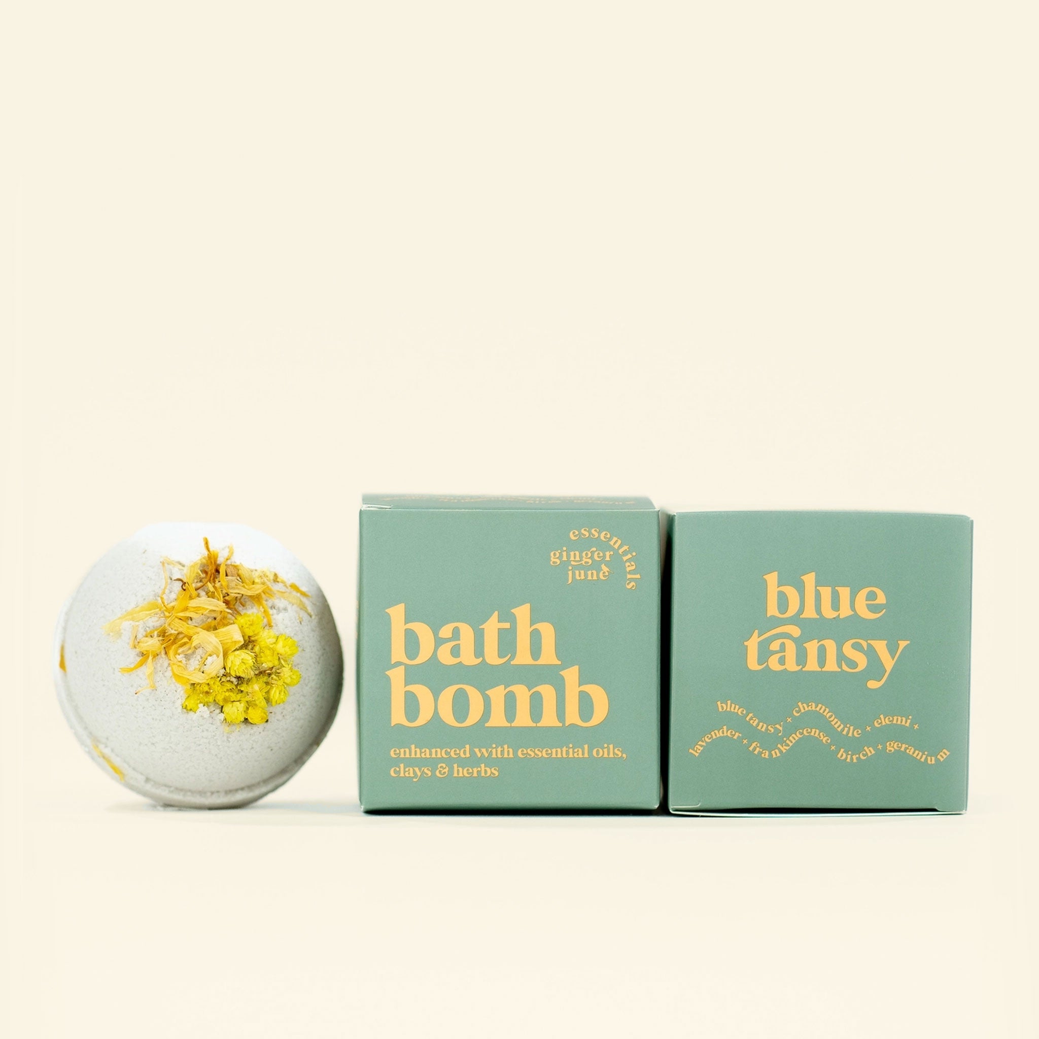 On a neutral background is a green bath bomb with a green box next to it that reads, &quot;bath bomb enhanced with essential oils, clays &amp; herbs&quot;