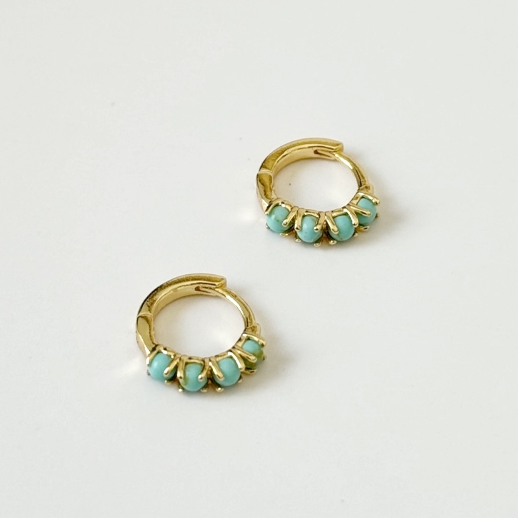 A pair of gold huggie hoops with turquoise stones along the front edge. 