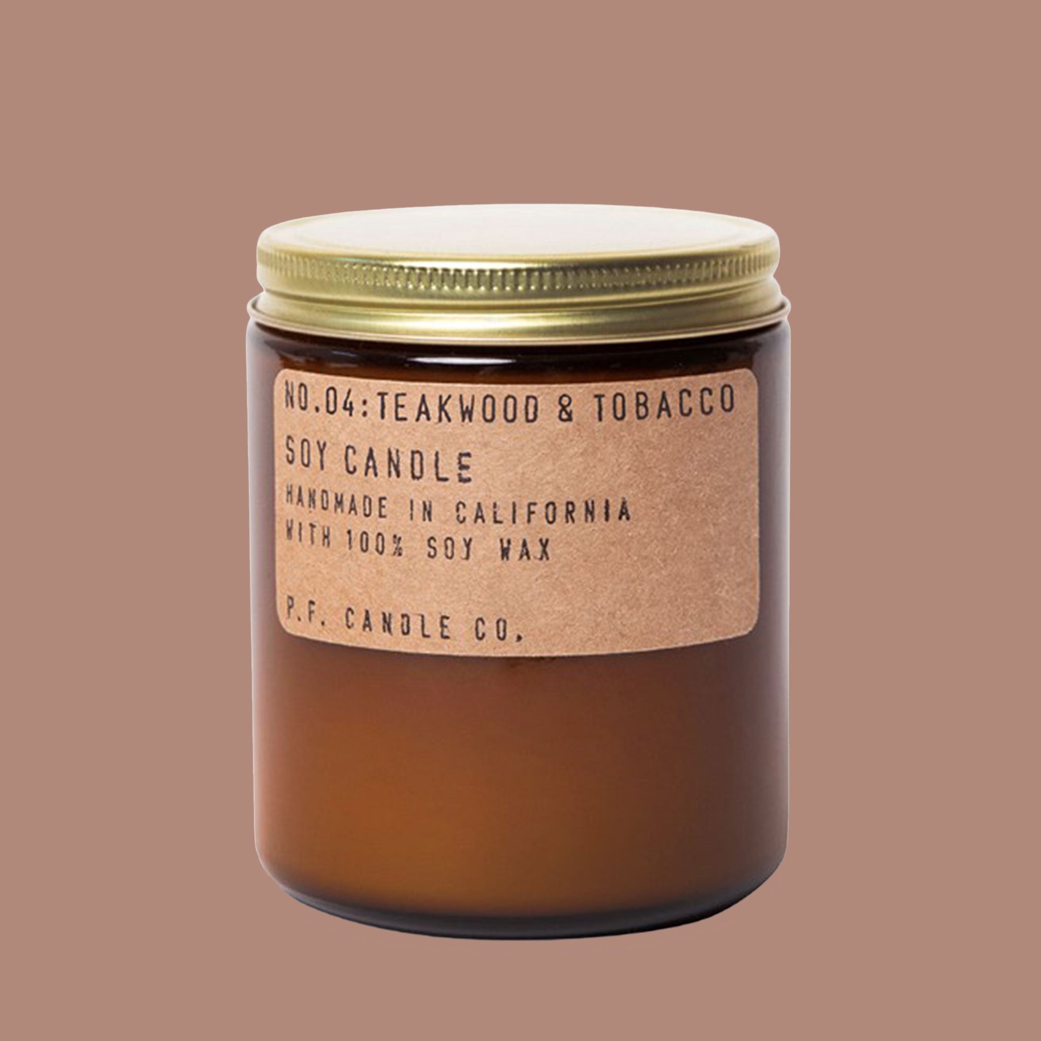 Against a white background is a dark amber, round jar. The jar has a gold lid. On the front of the jar is a brown, rounded, rectangular sticker with black text. The text reads ‘no.04 teakwood & tobacco. Soy candle. Handmade in California with 100% soy way. P.F. candle co.’