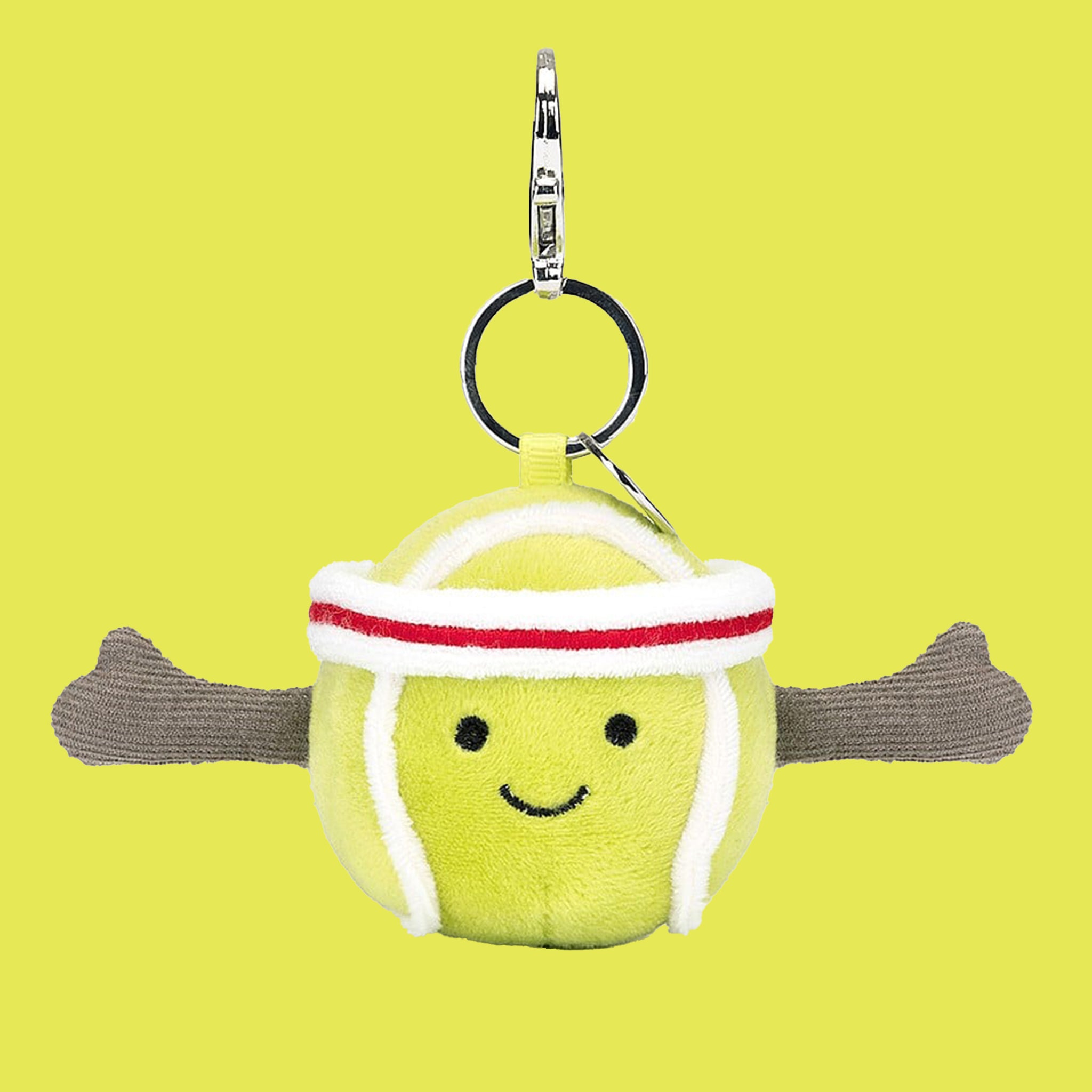 On a green background is a green tennis ball shaped bag charm with a smiling face and a silver loop for attaching. 