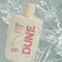 A cream colored bottle of sunscreen with red text that reads, 'Dune The Mug Guard Invisible Gel Sunscreen for Face'. 