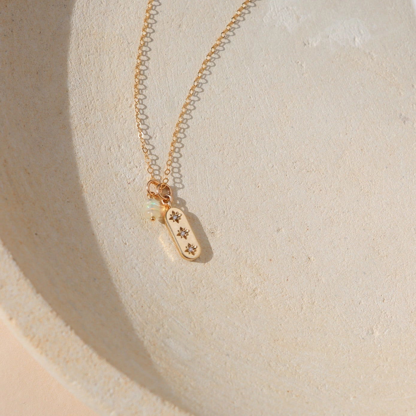 A gold necklace with 3 stones on it on a neutral ground.