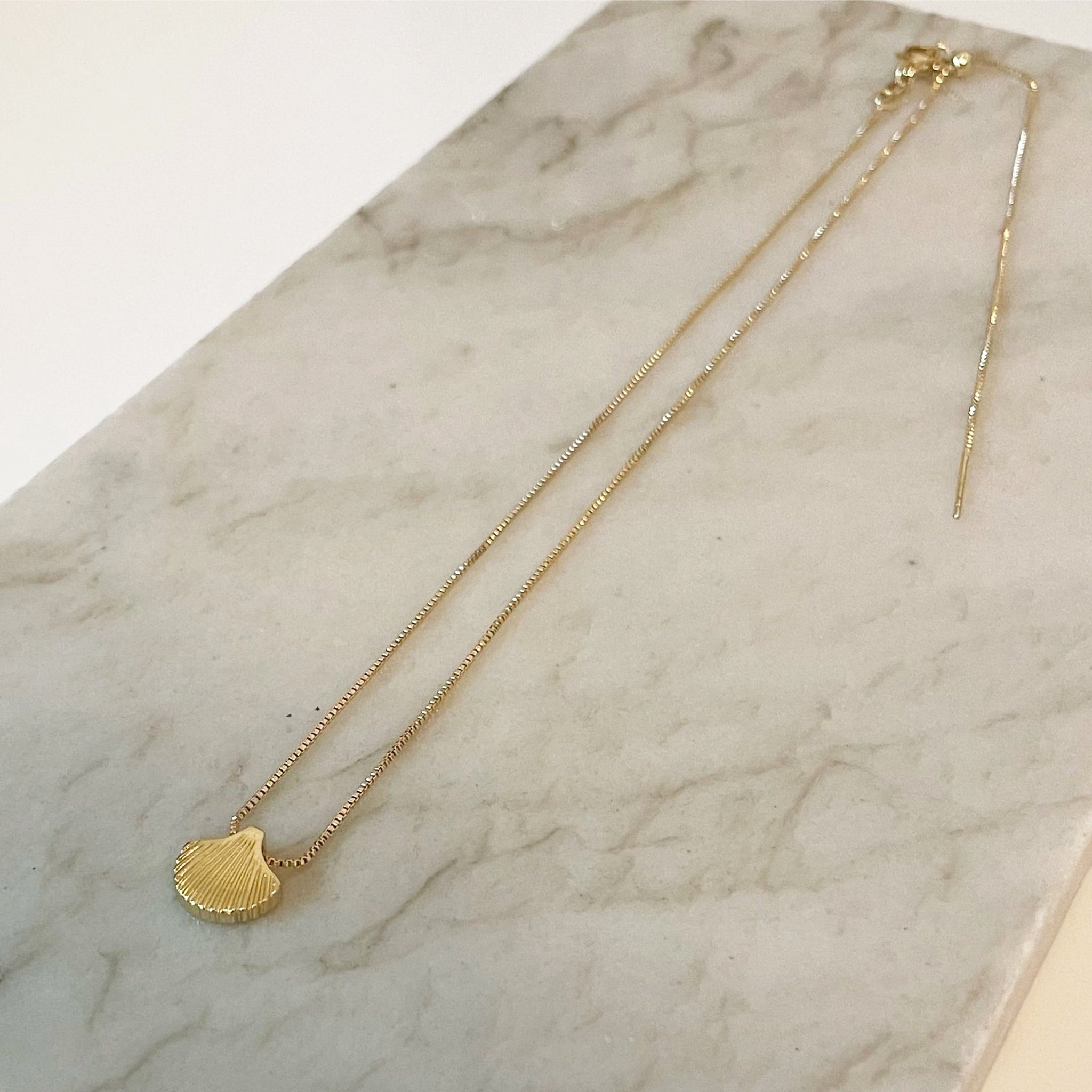 A gold chain necklace with a shell shaped charm. 