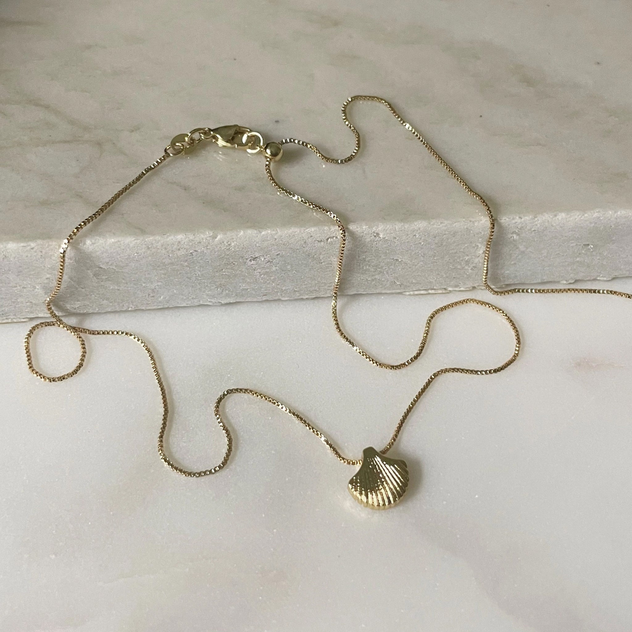 A gold chain necklace with a shell shaped charm. 