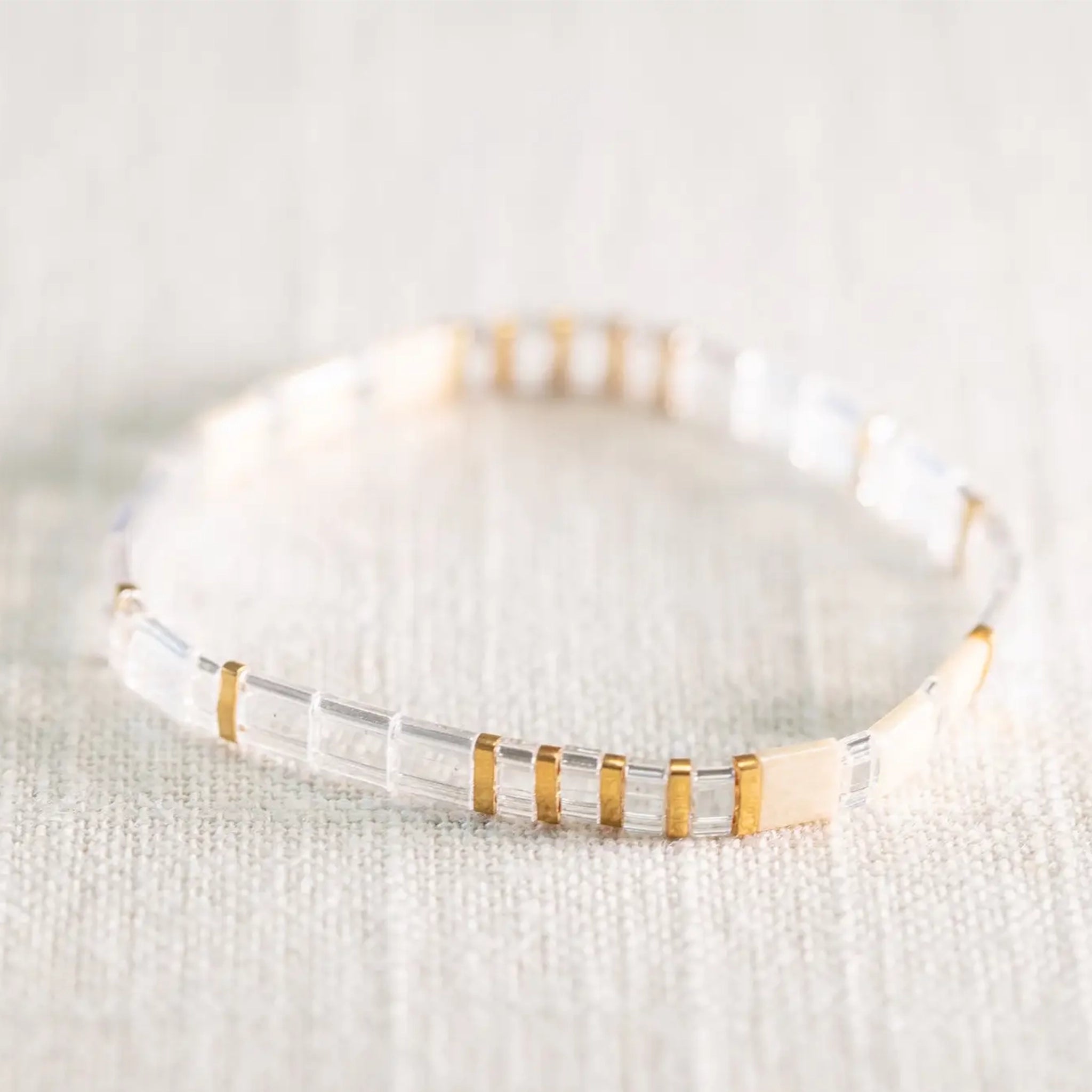 A clear and gold beaded bracelet on a neutral background. 