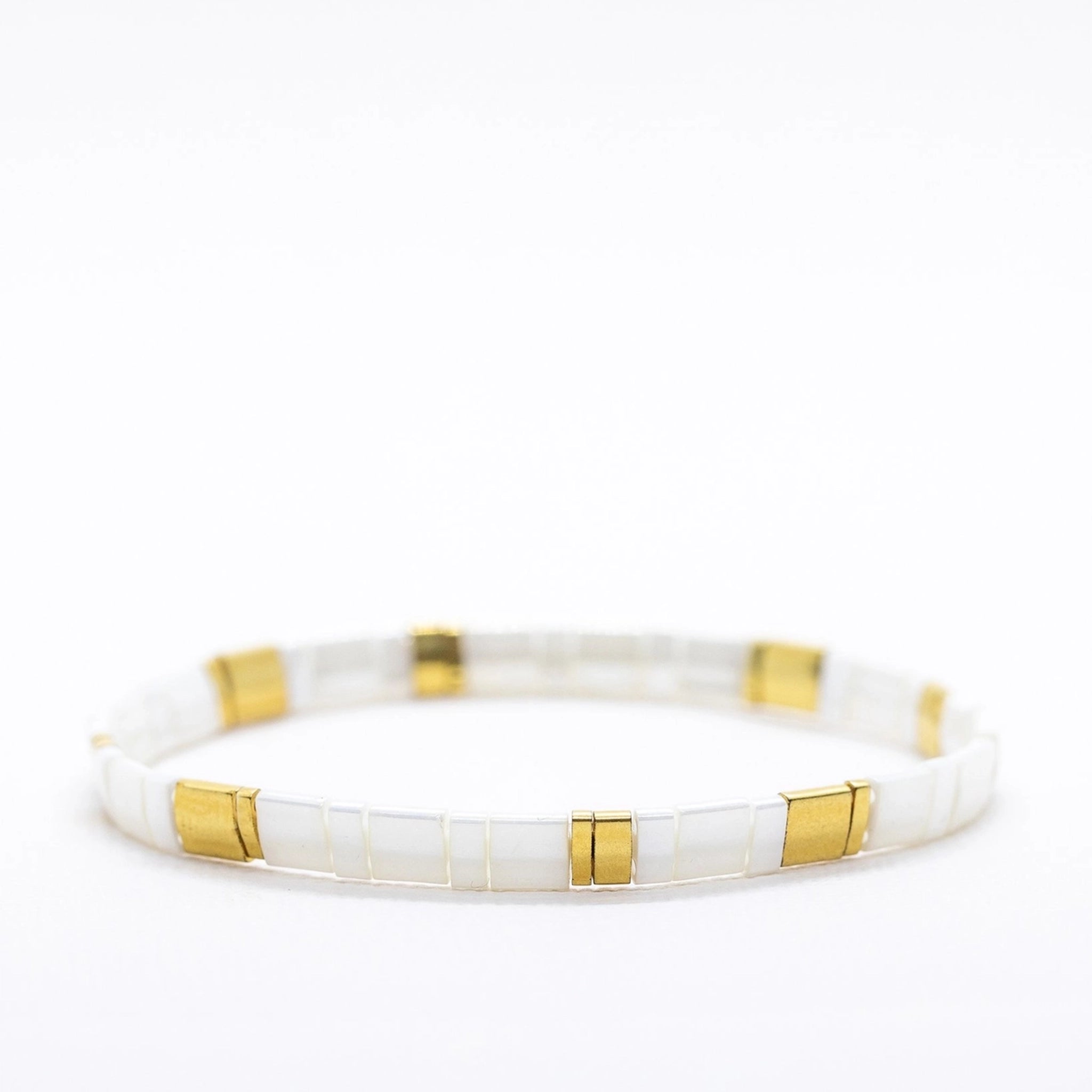 On a white background is a white and gold alternating bead bracelet. 