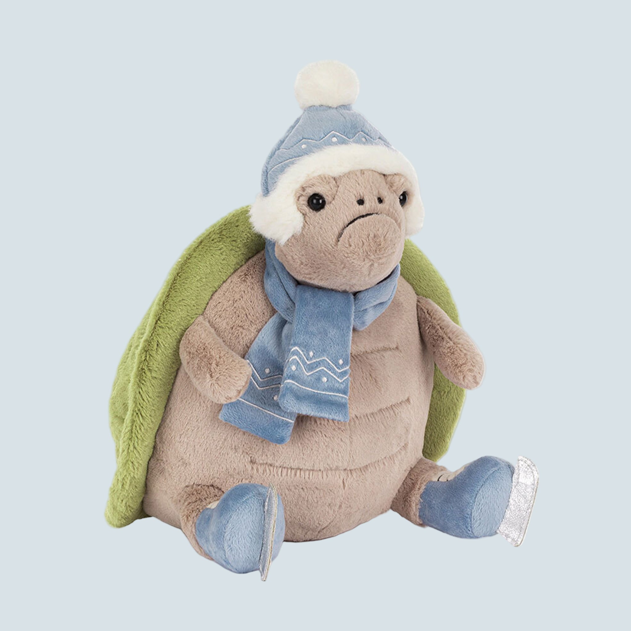 A turtle shaped stuffed animal toy wearing a scarf, ice skates and a beanie. 