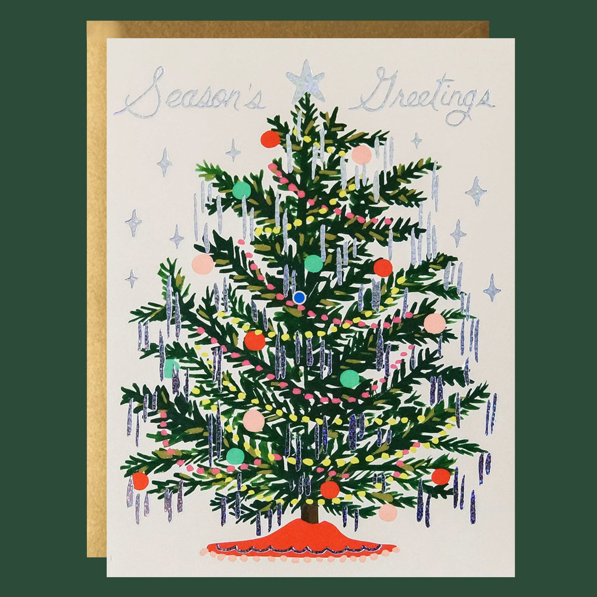 A cream colored card sits against a dark green background. On the front of the card there is a drawing of a dark green Christmas tree. There are yellow and red Christmas lights up and down the tree. There are green, red and pink ornaments spread out all over the tree. Silver tinsel is hanging on the end of each tree branch. At the bottom is a red tree skirt. At the top is a sliver star. Above the tree in silver script it reads ‘season's greetings.’ The card is accompanied by a white envelope.