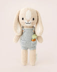 A neutral rabbit shaped stuffed animal that's wearing blue overalls with carrots in his pockets.