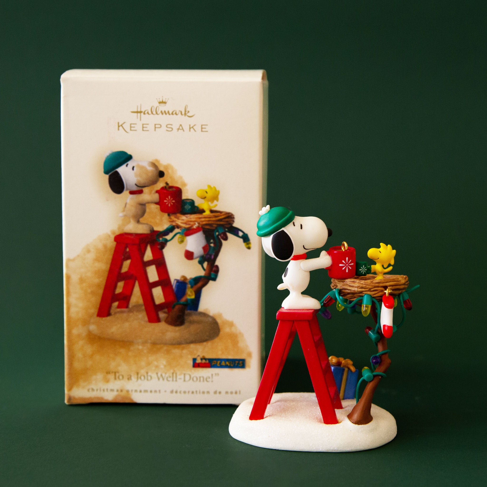 A Snoopy holiday ornament of him standing on a ladder with a string of lights. 