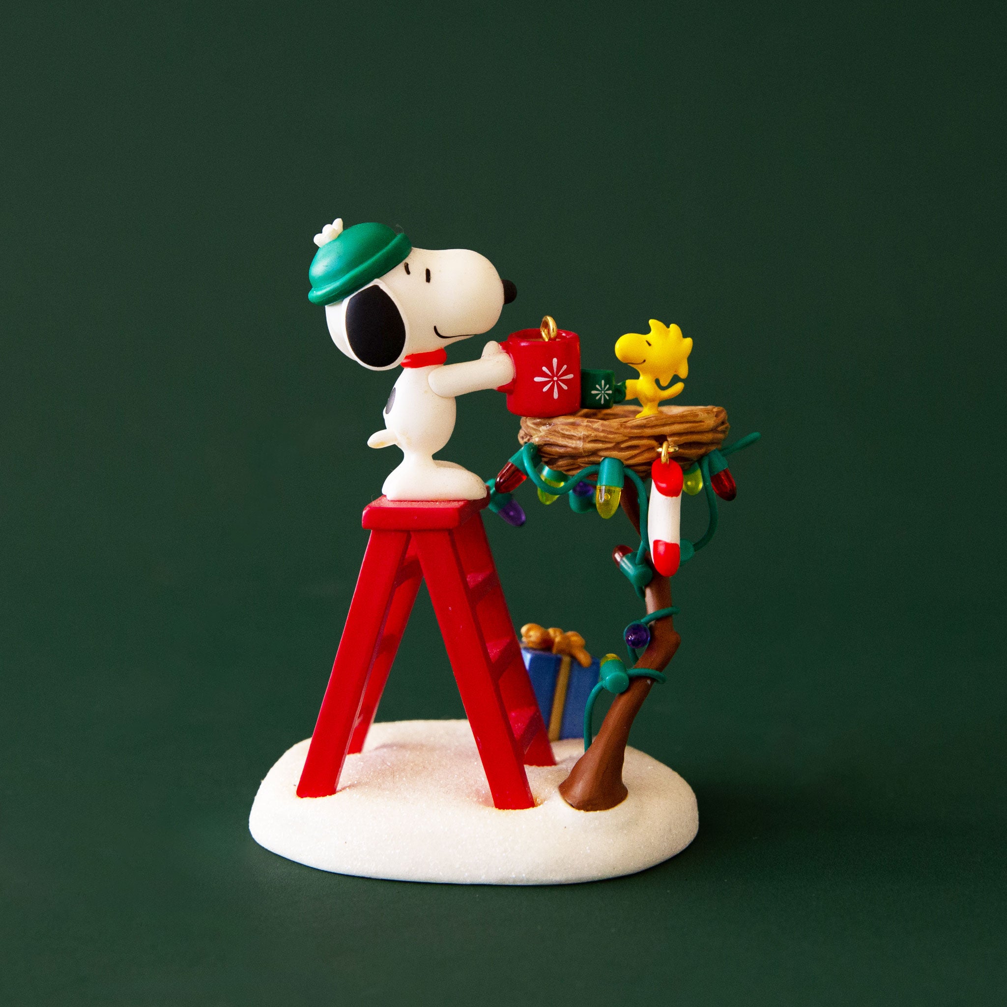 A Snoopy holiday ornament of him standing on a ladder with a string of lights. 