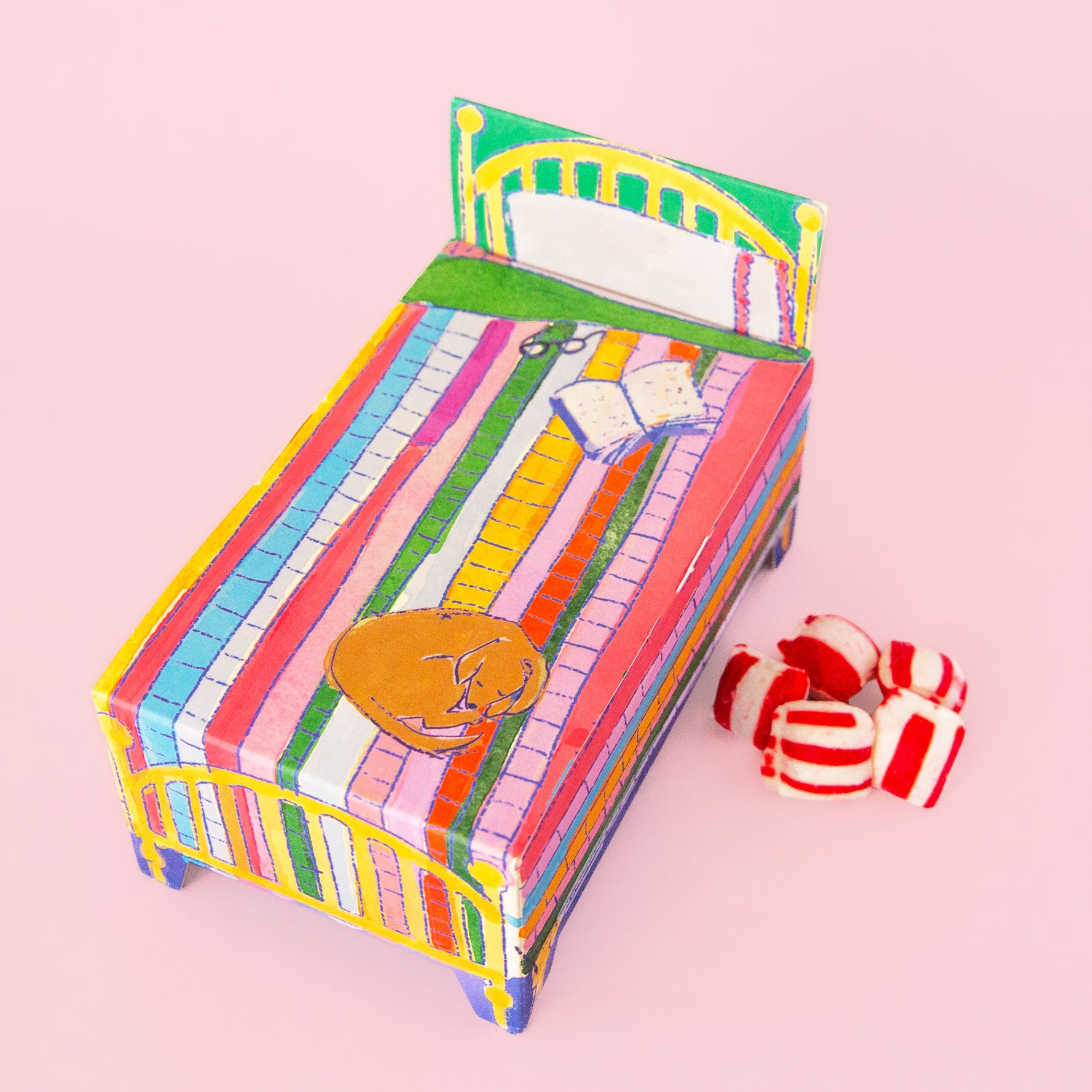 A multi colored box of candy with packaging the shape of a bed. 