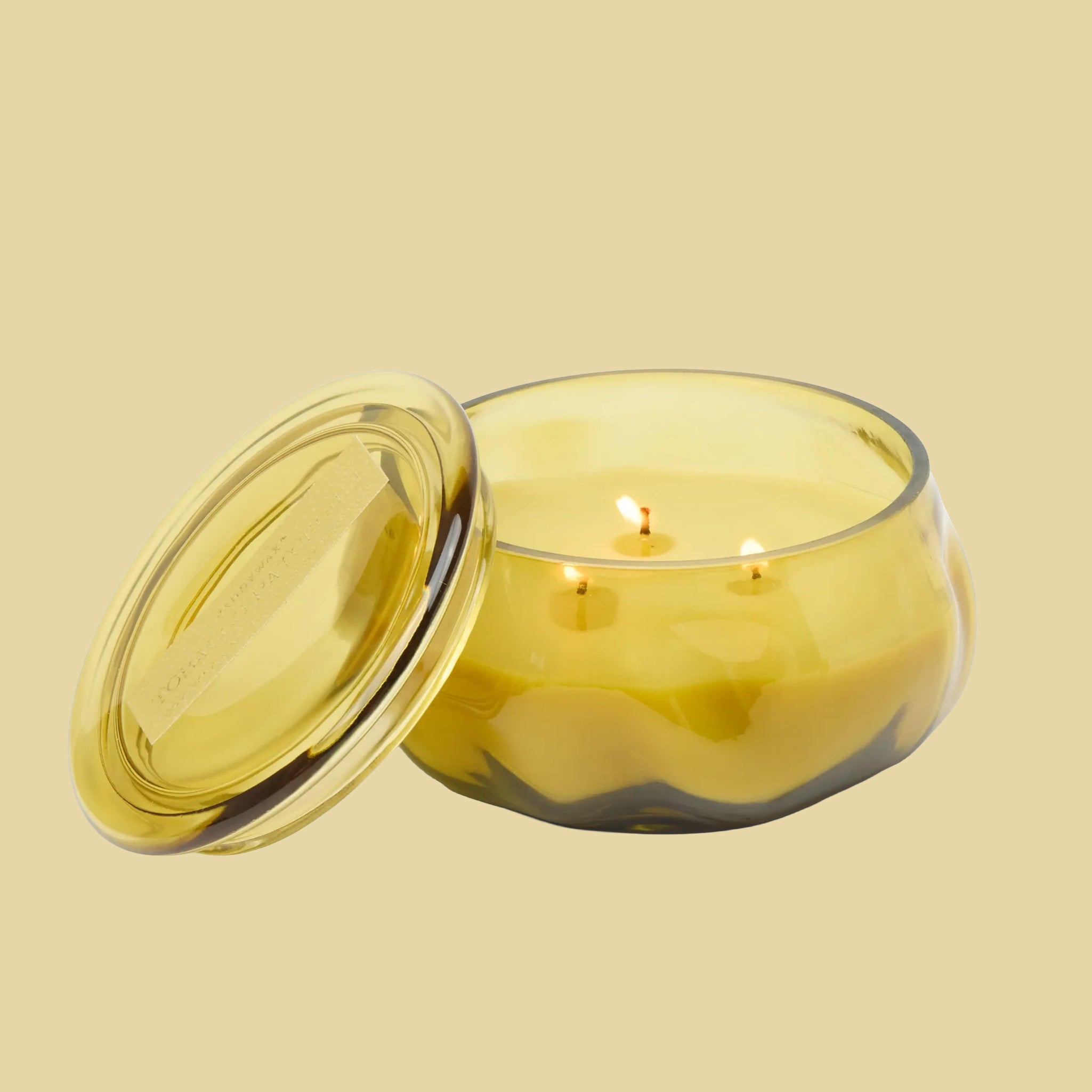 A yellow glass jarred candle with a lid. 
