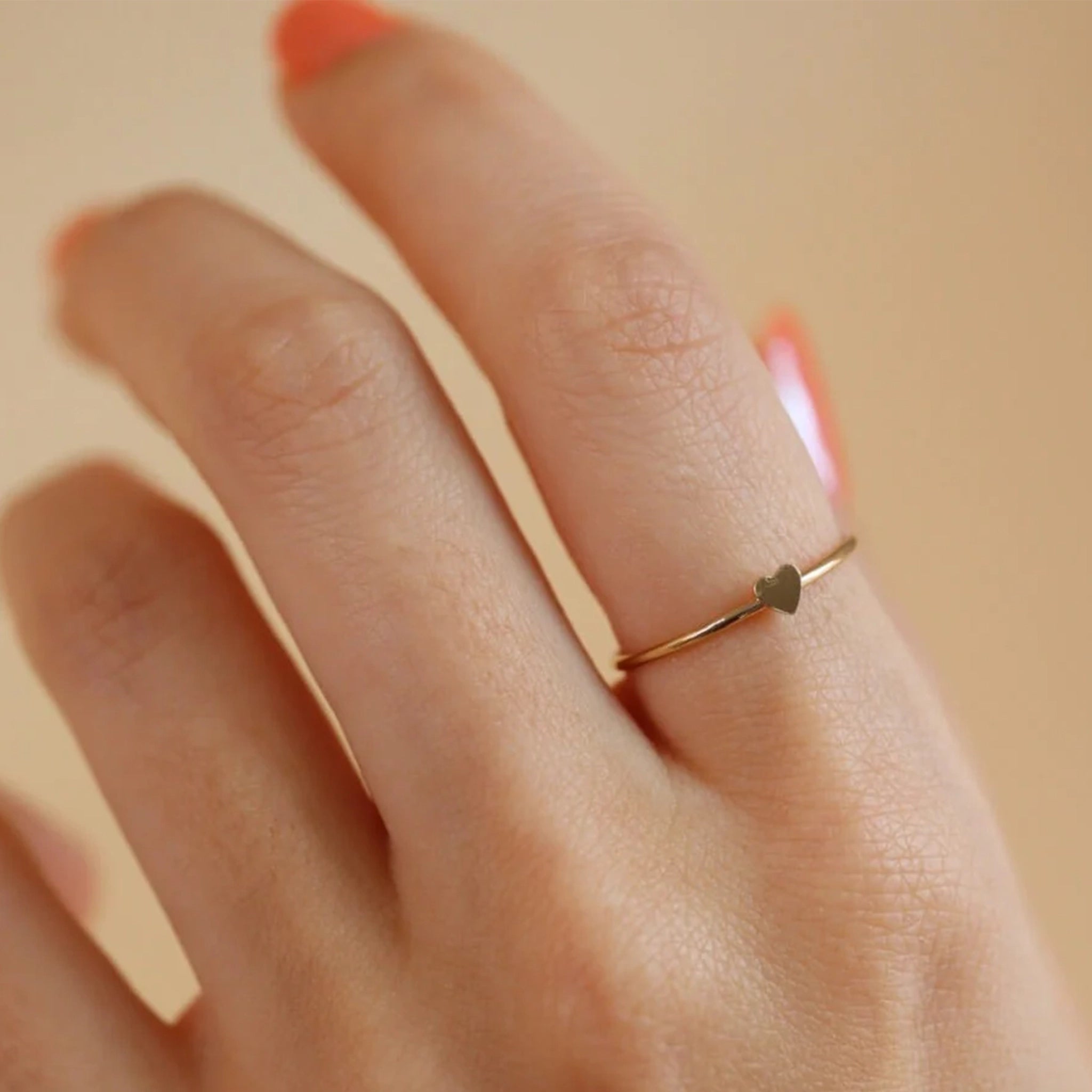On a models finger is the gold filled dainty tiny heart ring. 