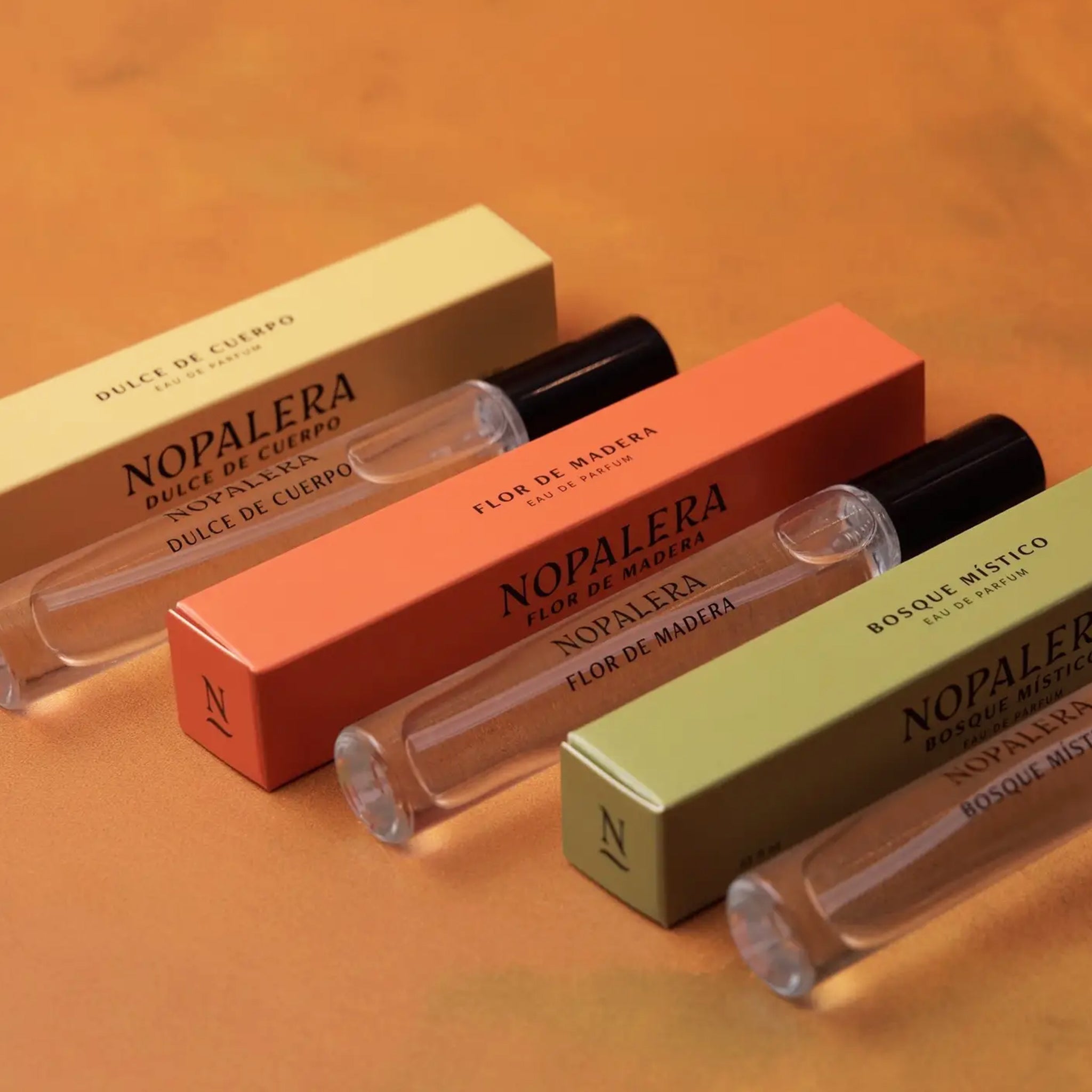 A set of three travel sized fragrances, one with a yellow box, one with an orange and one with a green. Each reads, "Nopalera". 