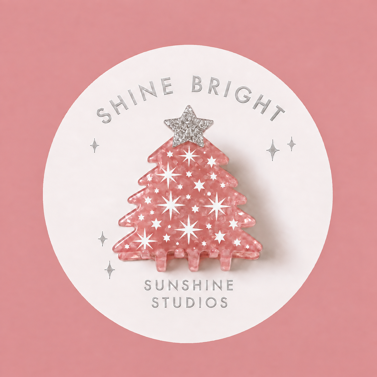 A pink Christmas tree-shaped mini hair clip with silver glittery snowflakes and a silver star topper, displayed on a white circular backing card that reads 'SHINE BRIGHT SUNSHINE STUDIOS' against a dusty pink background.