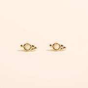 On a neutral background is a pair of stud earrings with a round white opal in the center. 