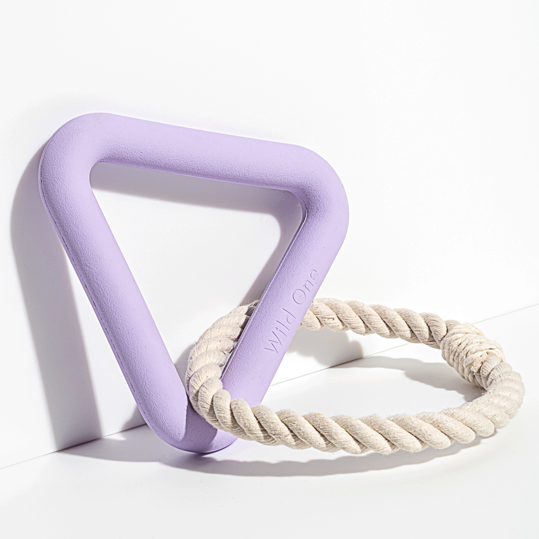 On a white background is a purple rubber triangle shaped dog toy with a cream loop rope around one of the corners. 