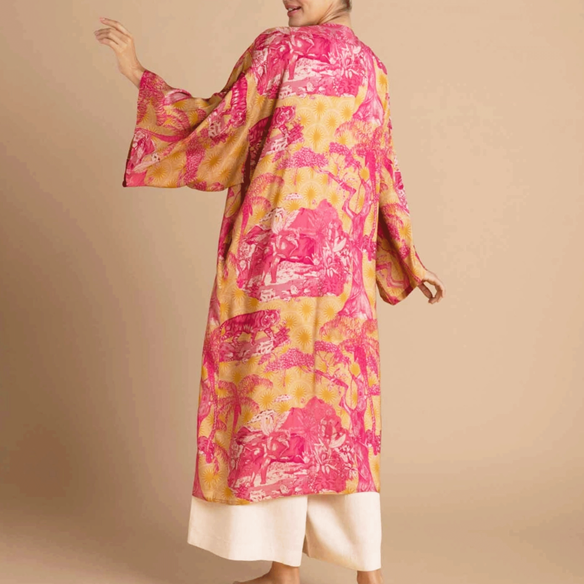 On a tan background is a model wearing a pink and yellow/orange robe with a tropical and floral print.