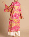 On a tan background is a model wearing a pink and yellow/orange robe with a tropical and floral print.