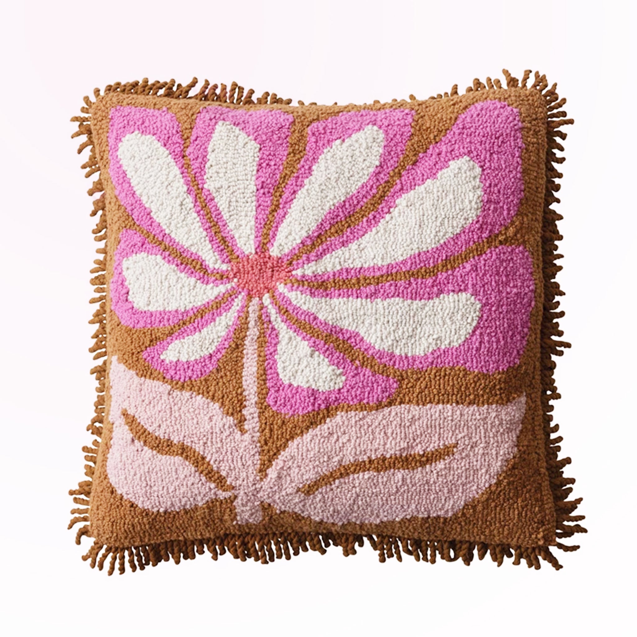 On a pink background is a tan, pink and white square pillow with a fringe edge and flower design.