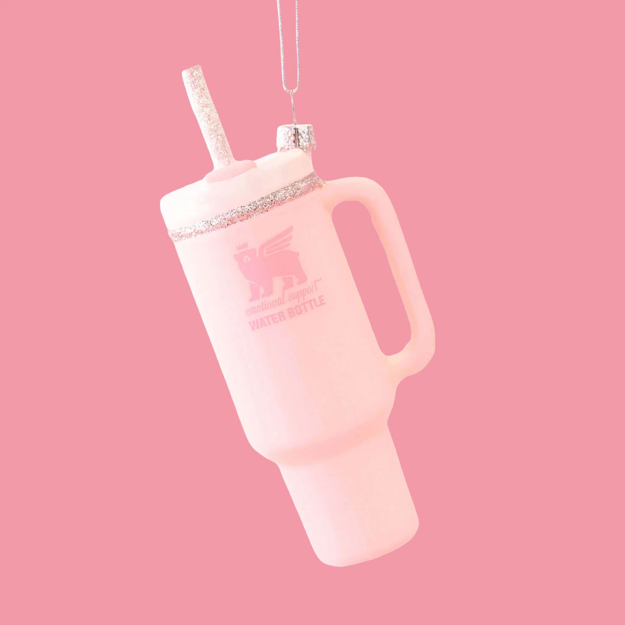 A pink drinking tumbler ornament shown against a pink background. The lid and straw have silver sparkle details. 