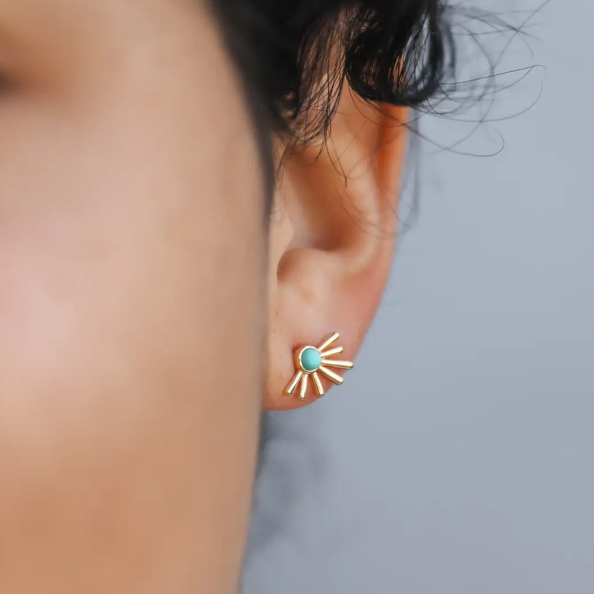 A pair of sunburst shape gold earrings with a turquoise stone in the center.