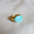 A gold chunky ring with an oval turquoise stone in the center. 