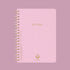 A light lilac colored notebook that is spiral bound and reads, 'Notebook' in gold foiled text. 