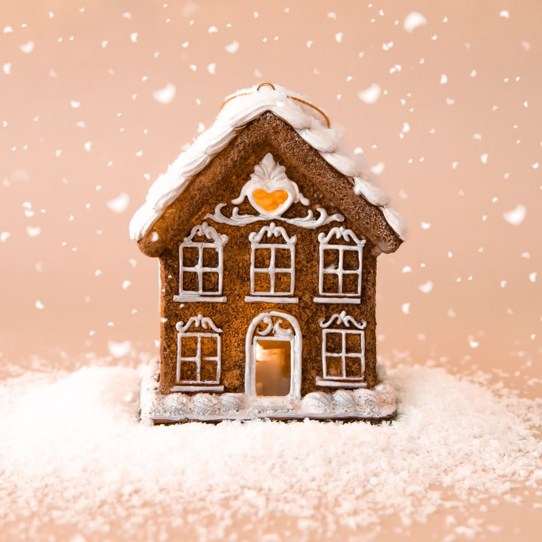 A gingerbread house shaped ornament with white pipping details and lights coming from the inside. 