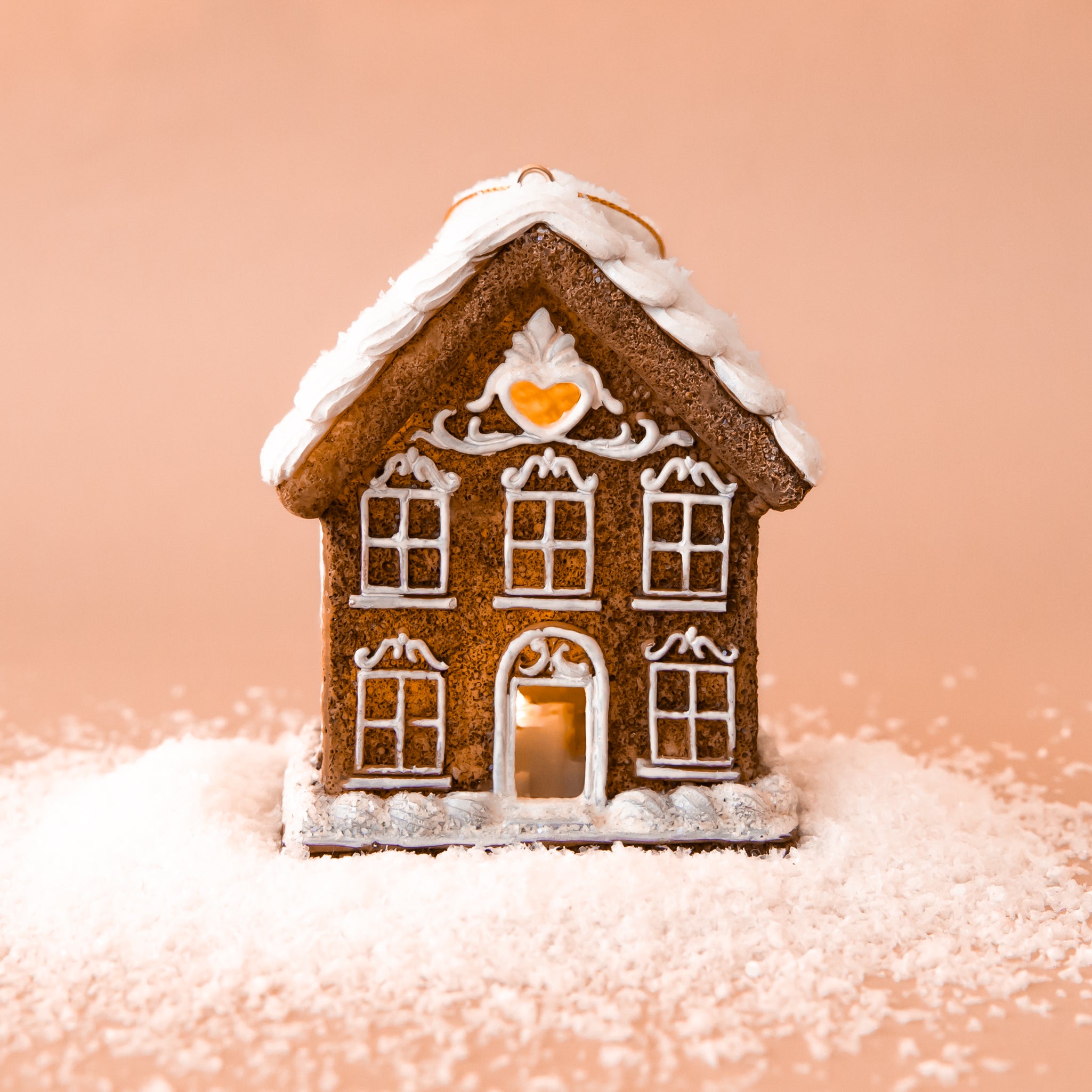 A gingerbread house shaped ornament with white pipping details and lights coming from the inside. 