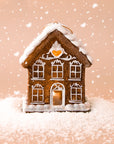 A gingerbread house shaped ornament with white pipping details and lights coming from the inside. 