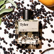 A clear glass bottle of cologne with black wooden cap and a label that reads, 'Tyler'. 